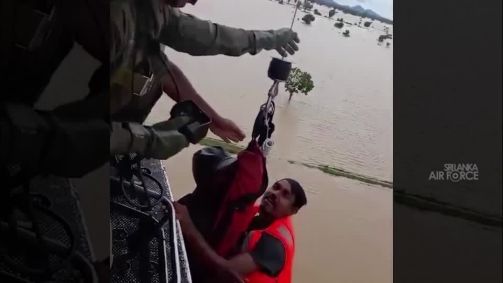 Homens de colete laranja resgatam um outro homem da enchentes