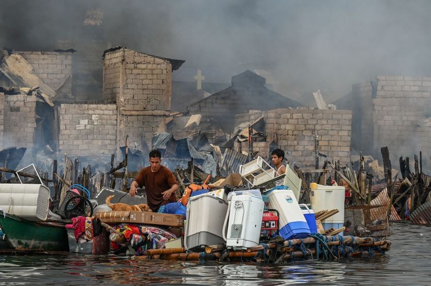 Pessoas carregam pertences em jangada improvisada durante um incêndio em Tondo, Manila • Jam Sta Rosa/AFP/Getty Images via CNN Newsource 25 Nov 24