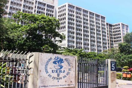 Fachada do prédio da UERJ. Há uma placa na frente destacando o nome da instituição.
