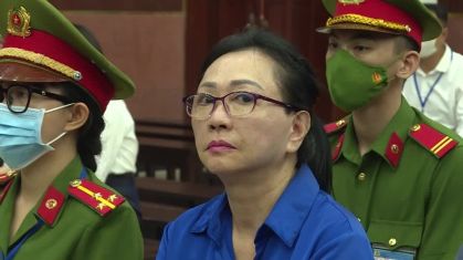 Soldados uniforme e chapéu verde militar e detalhes vermelhos, no centro uma mulher com óculos, cabelos presos e camisa azul escura