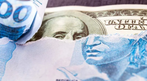 Nota de 100 reais rasgada no topo revela uma nota de 100 dólares ao fundo