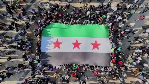 Pessoas segurando bandeira verde branca e preta que contém três estrelas vermelhas
