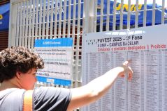Um menino busca seu nome em uma lista fixada em um portão de universidade, onde aconteceu a segunda fase da Fuvest