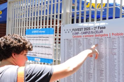 Um menino busca seu nome em uma lista fixada em um portão de universidade, onde aconteceu a segunda fase da Fuvest
