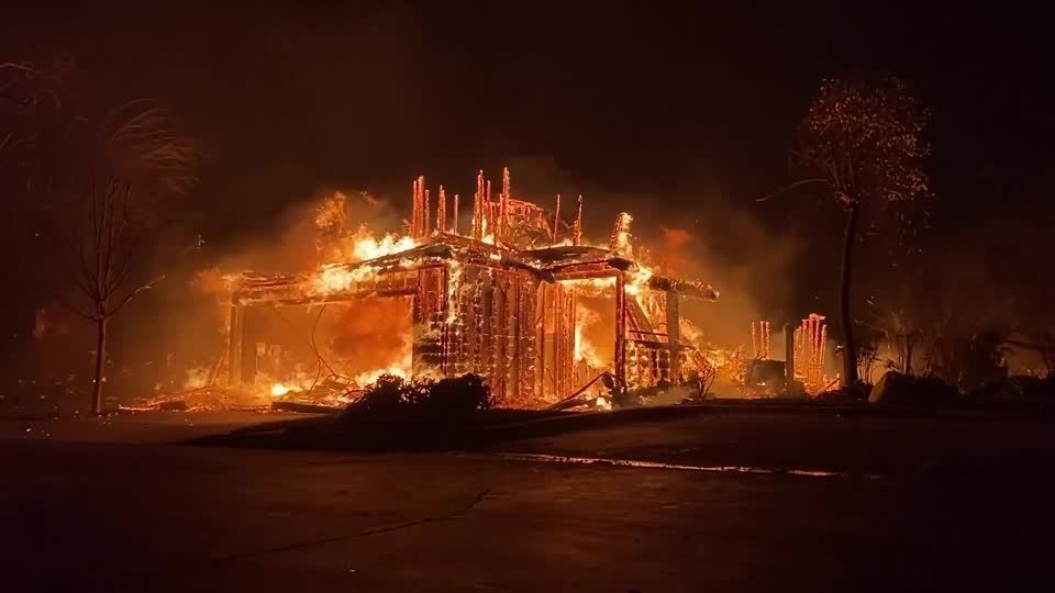 Imagem mostra estrutura de casa destruída em meio a chamas de noite.