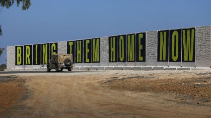 Veículo militar de Israel passa em frente a cartaz que pede volta de reféns feitos pelo Hamas perto da fronteira com Gaza