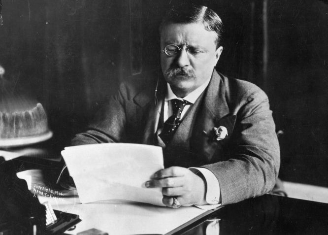 Theodore Roosevelt (1858 - 1919), o 26º presidente dos Estados Unidos (1901-09) sentado em sua mesa trabalhando. • Hulton Archive/Getty Images