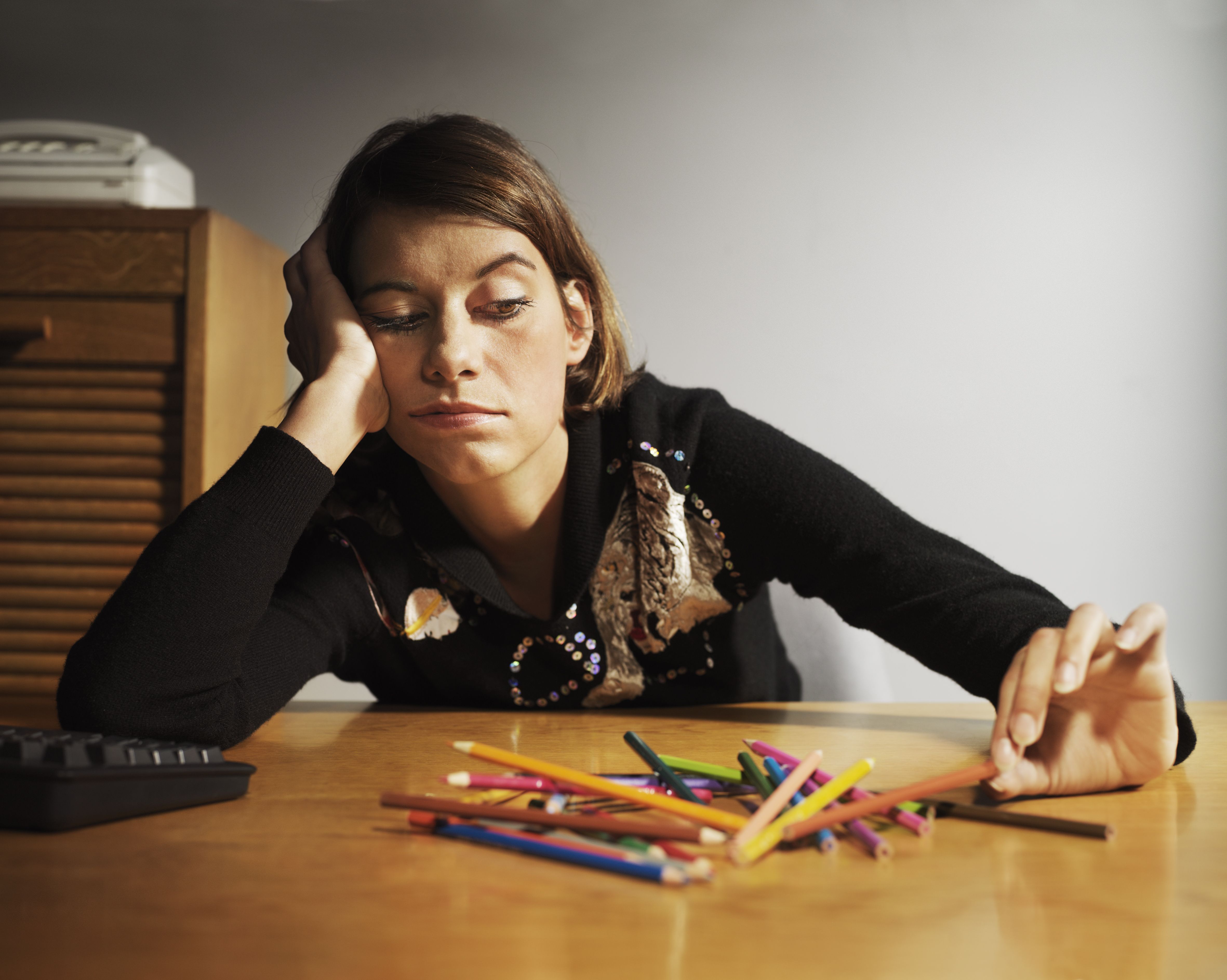Woman at desk playing with coloured pencils, head in hand