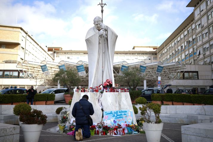Homem reza perto de estátua do papa João Paulo 2º no Hospital Gemelli, em Roma, onde o papa Francisco está internado. • Reuters/Alkis Konstantinidis