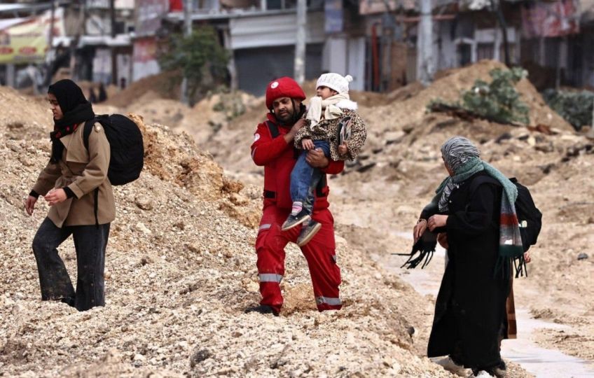 Funcionário da Sociedade do Crescente Vermelho Palestino carregando uma criança em meio a escombros. • Reprodução/Sociedade do Crescente Vermelho Palestino