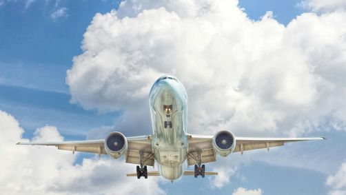 Avião decolando. O céu está azul e há nuvens.