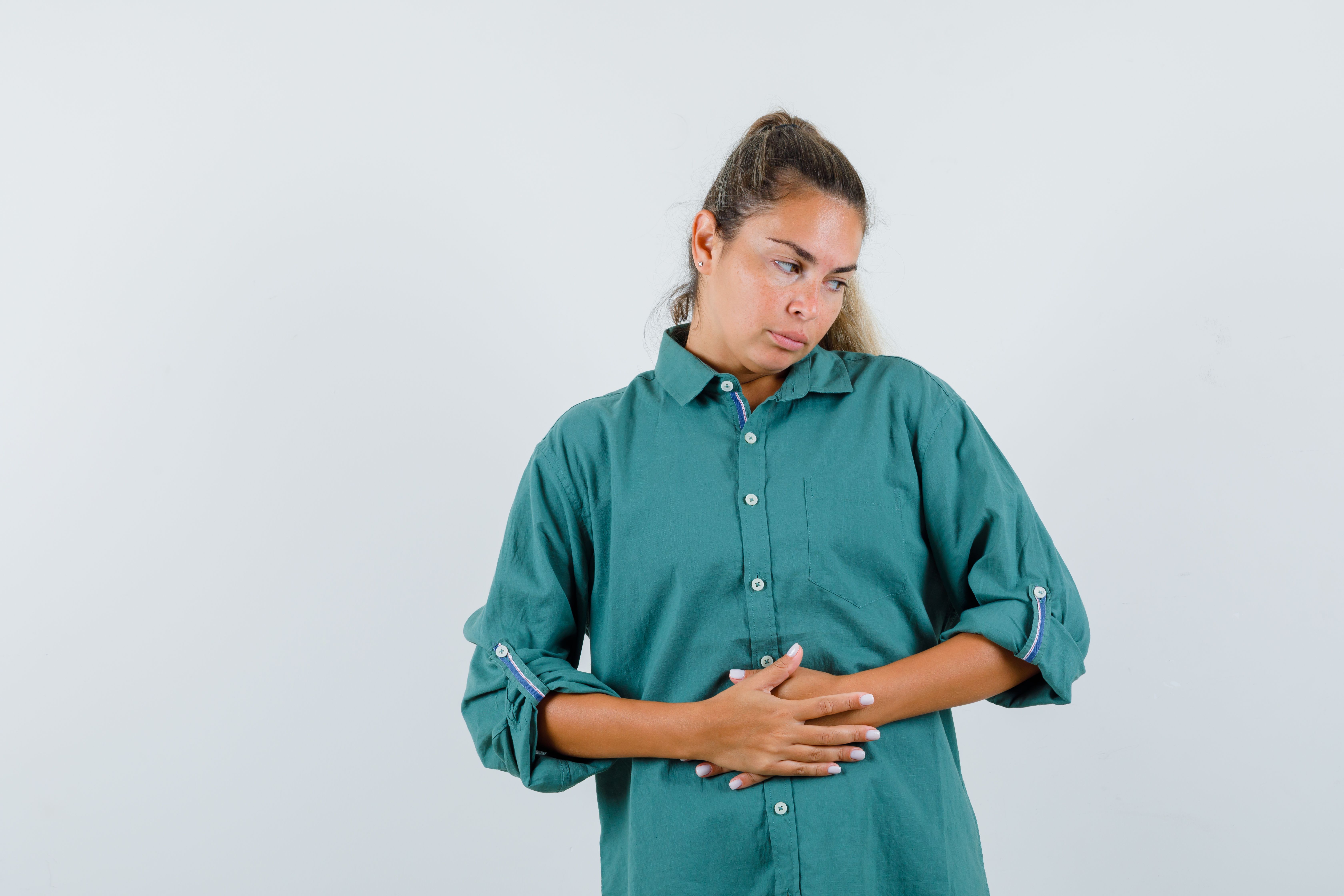young female in blue shirt holding hands on her belly and looking tedious , front view.