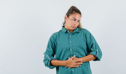 young female in blue shirt holding hands on her belly and looking tedious , front view.