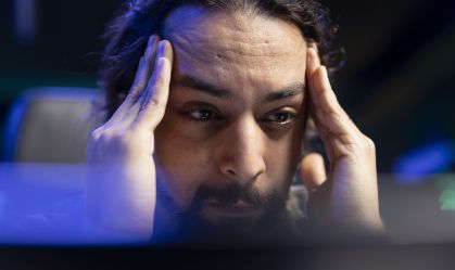 Man rubs his temple and looks at laptop