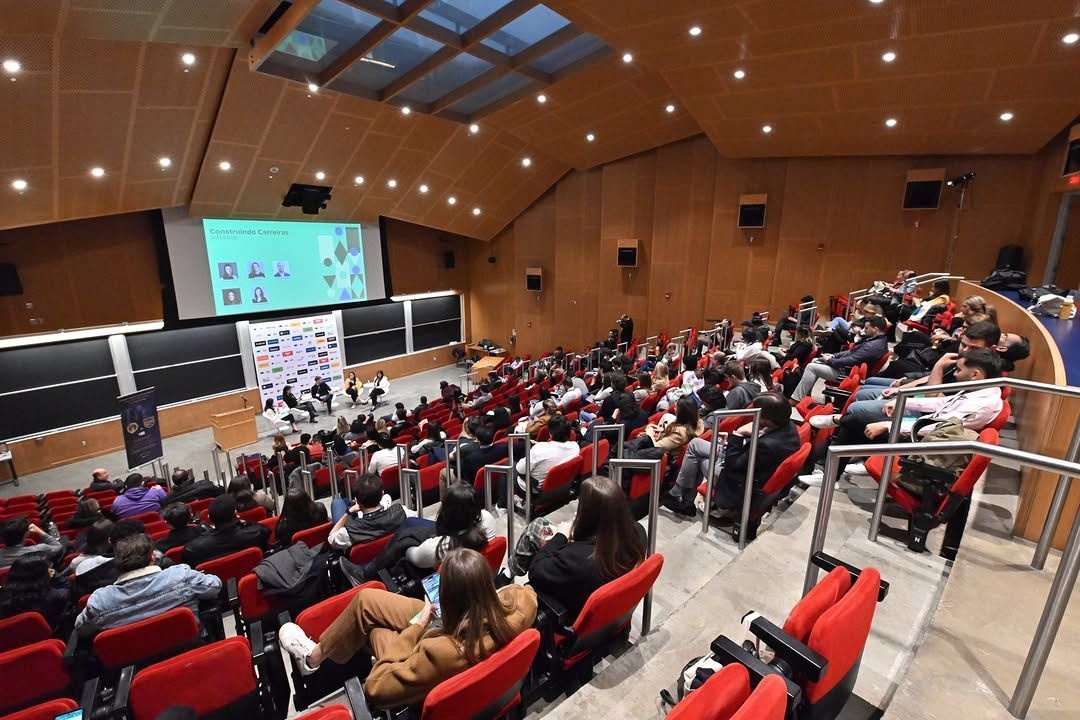 Auditório com todas as cadeiras ocupadas. Há um telão em cima de um palco.