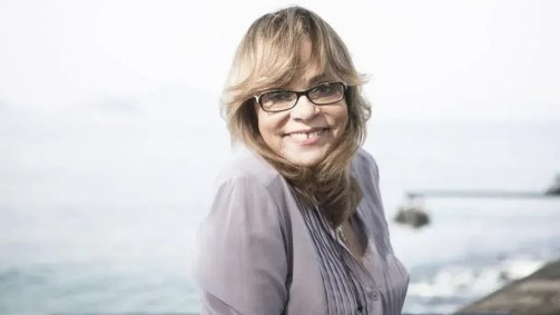 A autora de novelas Gloria Perez. Ela está sorrindo. Usa óculos e é loira.