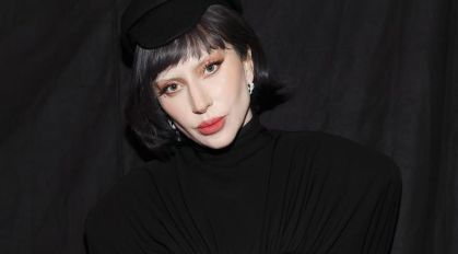 Lady Gaga. Ela está com um chapéu preto. A roupa dela também é preta