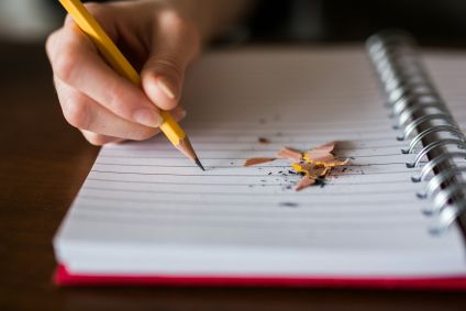Pessoa escrevendo em um caderno. Há ponta de lápis em cima da folha