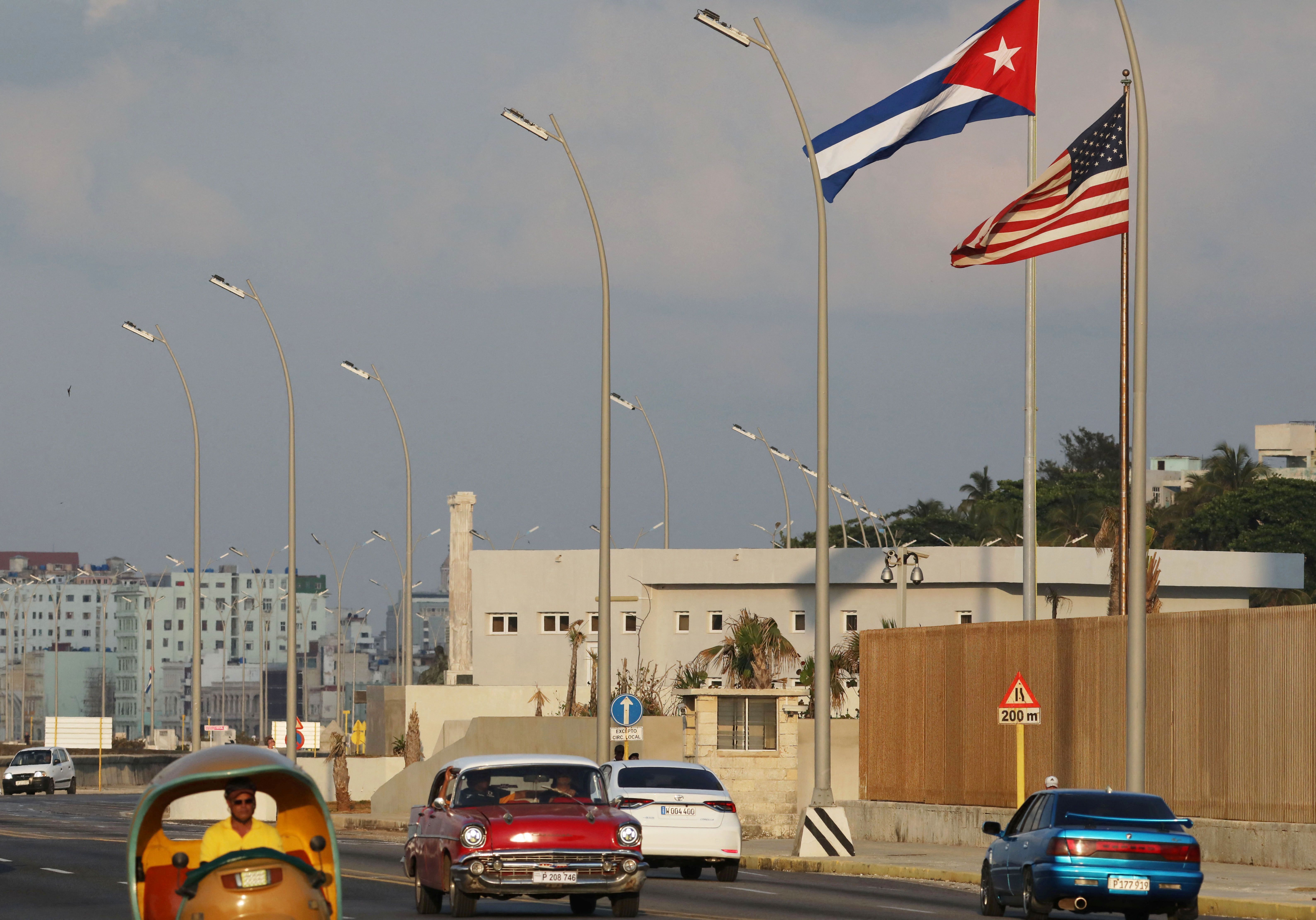 Carros passam por bandeiras cubana e americana ao lado da Embaixada dos EUA em Havana, Cuba