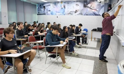 Alunos na sala de aula; professor escrevendo na lousa