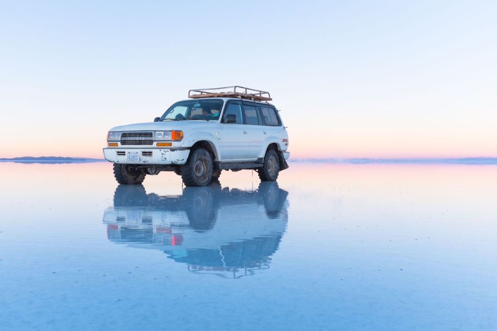 A imagem mostra um carro refletindo na superfície do Salar de Uyuni.