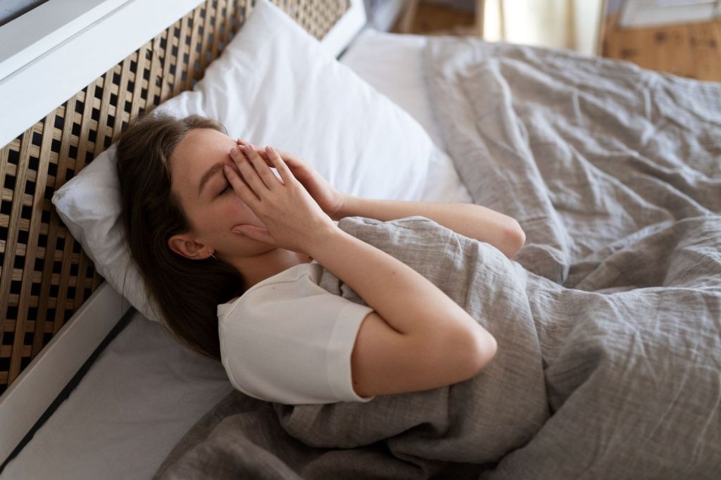 A imagem mostra uma mulher acordando em uma cama com as mãos no rosto.