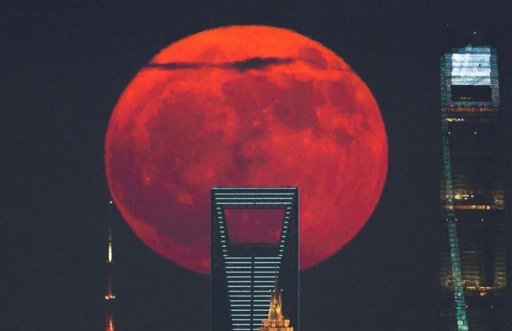 Lua de Sangue surgindo atrás dos arranha-céus da cidade, por Tianyao Yang. Esta fotografia captura uma Lua cheia vermelha nascendo ao lado dos arranha-céus mais altos de Xangai, em Lujiazui. Imagem de arquivo • TianyaoYang