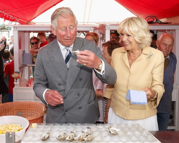 Príncipe Charles, príncipe de Gales, come uma ostra enquanto Camilla, duquesa da Cornualha, observa durante sua visita ao Festival de Ostras de Whitstable em 29 de julho de 2013 em Whitstable, Inglaterra. • Max Mumby/Indigo/Getty Images