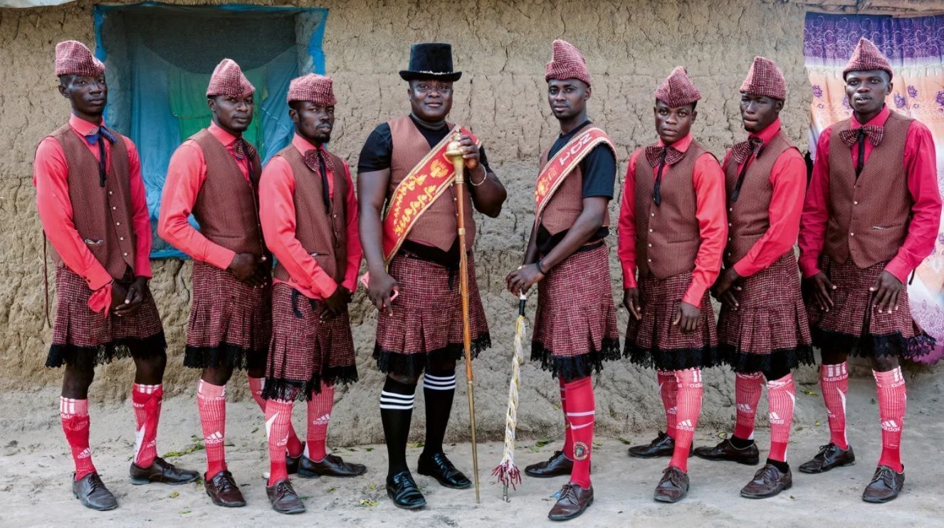 Benjamin Aidoo (ao centro, de chapéu preto) posa ao lado de alguns de seus dançarinos em seu uniforme "Scottish Red" em 2022. Tschumi descreve Aidoo como um de seus melhores amigos e uma figura chave para abrir-lhe as portas na documentação das singulares tradições funerárias de Gana • Reprodução/Regula Tschumi