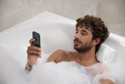 Homem na banheira segurando o celular.