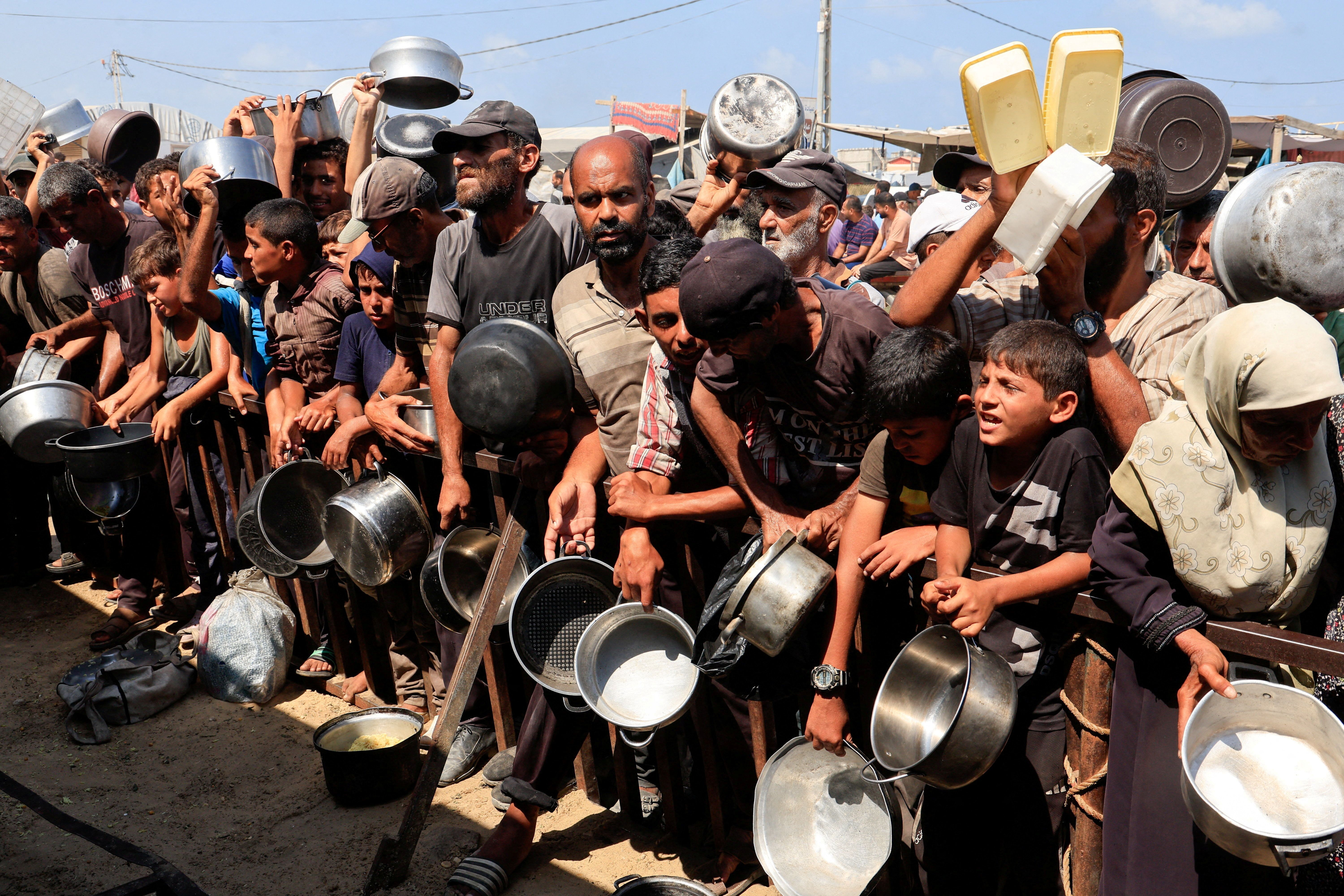 Palestinos seguram potes e recipientes enquanto esperam comida de cozinha de caridade em Khan Younis, sul da Faixa de Gaza 21/08/2025 REUTERS/Hatem Khaled