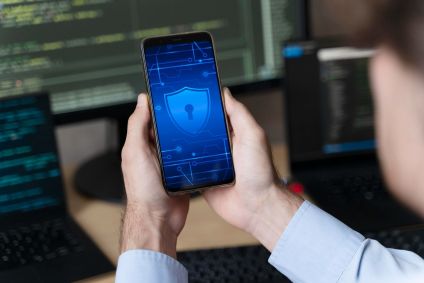 A imagem mostra uma pessoa segurando um smartphone com as duas mães, e a tela mostra um símbolo de segurança digital.