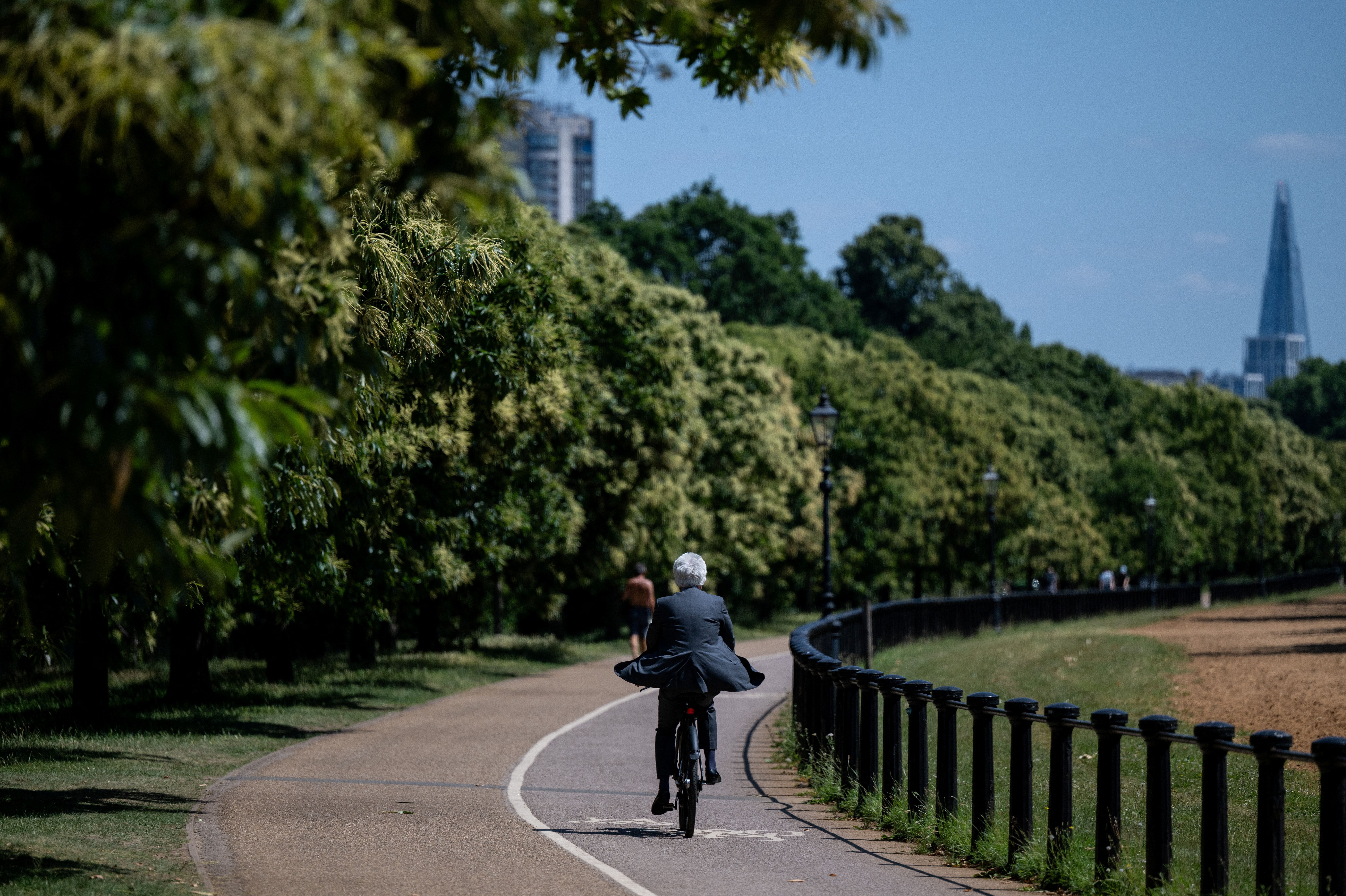 Homem de terno anda de bicicleta pelo Hyde Park em um dia quente de verão, em Londres