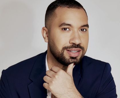Gil do Vigor posa para foto usando um terno azul, camiseta branca e com relógio em um dos braços