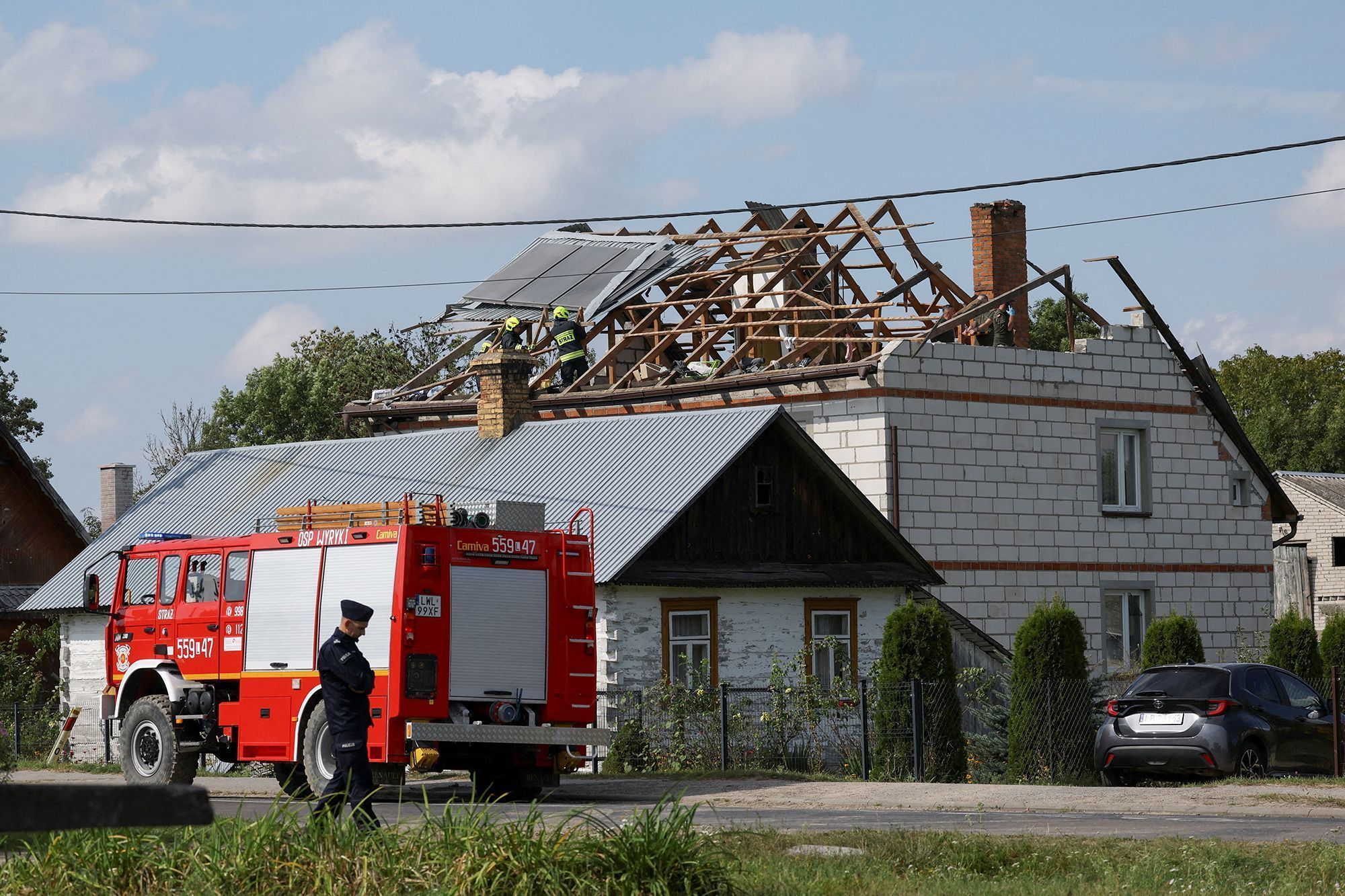 Um policial espera enquanto bombeiros trabalham no telhado destruído de uma casa, depois que drones russos violaram o espaço aéreo polonês durante um ataque à Ucrânia, com alguns sendo abatidos pela Polônia com o apoio de seus aliados da OTAN