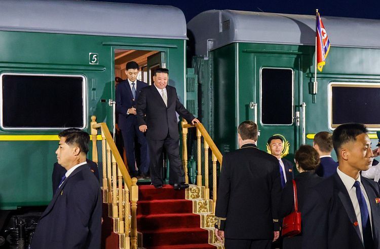 Imagem mostra Kim Jomg-un de terno preto desembarcando de um trem verde com a um faixa horizontal amarela