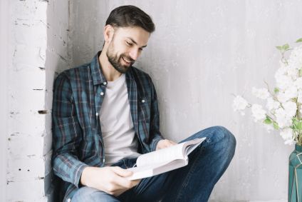 Rapaz está sentado em um canto de uma sala com um livro nas mãos