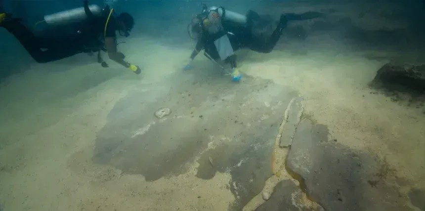 Membros da equipe de mergulho retiram areia de um piso polido que fazia parte do porto • National Geographic via CNN Newsource