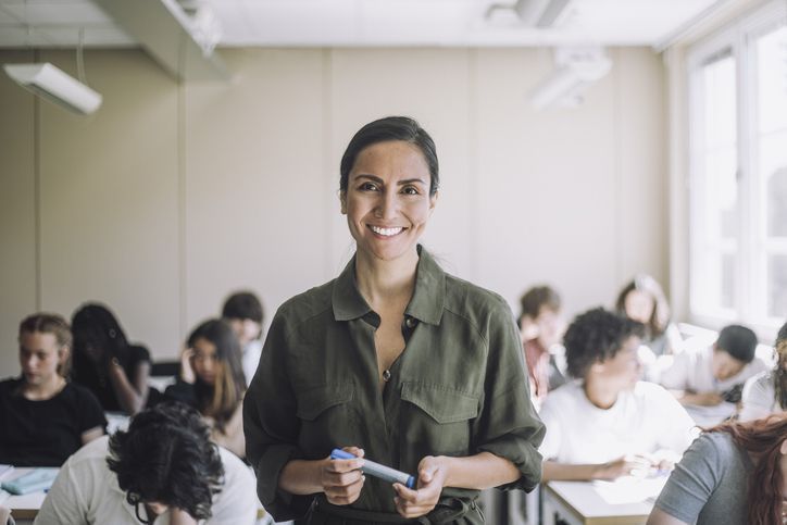 Portrait of happy female teacher with students in background at school