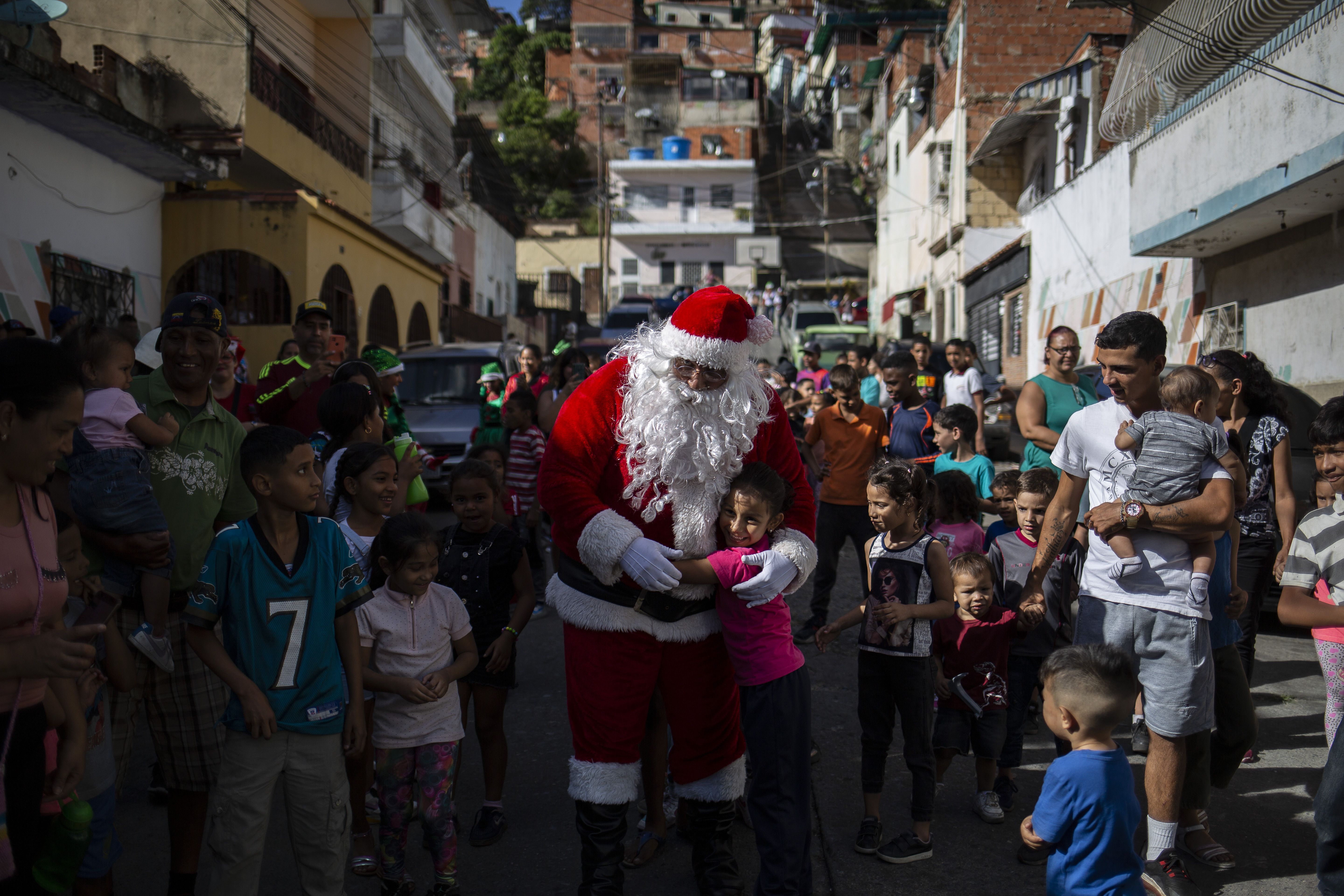 Um homem vestido de Papai Noel cumprimenta crianças da comunidade Barrio Las Palmas de El Cementerio, durante uma caminhada para visitar crianças e distribuir brinquedos em áreas pobres de Caracas, na Venezuela, durante o Natal
