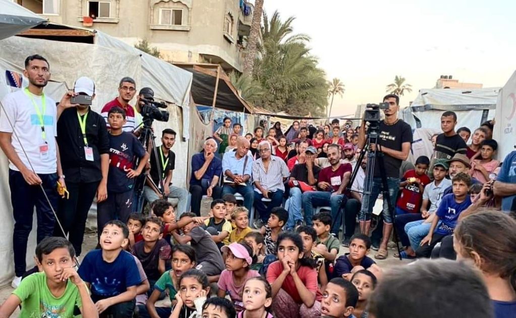 Palestinos assistem exibição de filme do Festival Internacional de Cinema de Jerusalém, em Gaza, em 2024. Organizadores esperam receber cerca de 300 pessoas por dia na primeira edição do Festival Internacional de Cinema de Mulheres de Gaza, a partir de 26 de outubro.