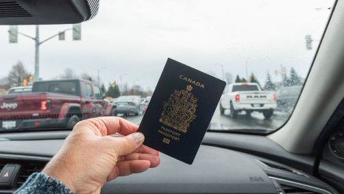 A mão de um passageiro segura um passaporte canadense enquanto viaja de carro em direção à fronteira entre Canadá e EUA.