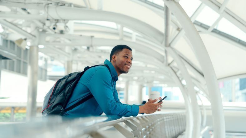Young African professional leaning on railing with smartphone in modern city