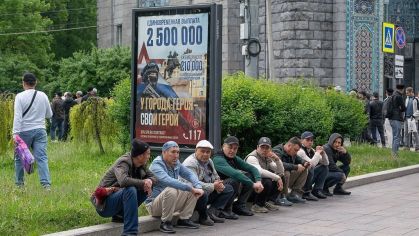 Muçulmanos sentados perto de um cartaz de recrutamento militar ao lado da Mesquita Catedral, em São Petersburgo, aguardando o início das orações do Eid al-Adha