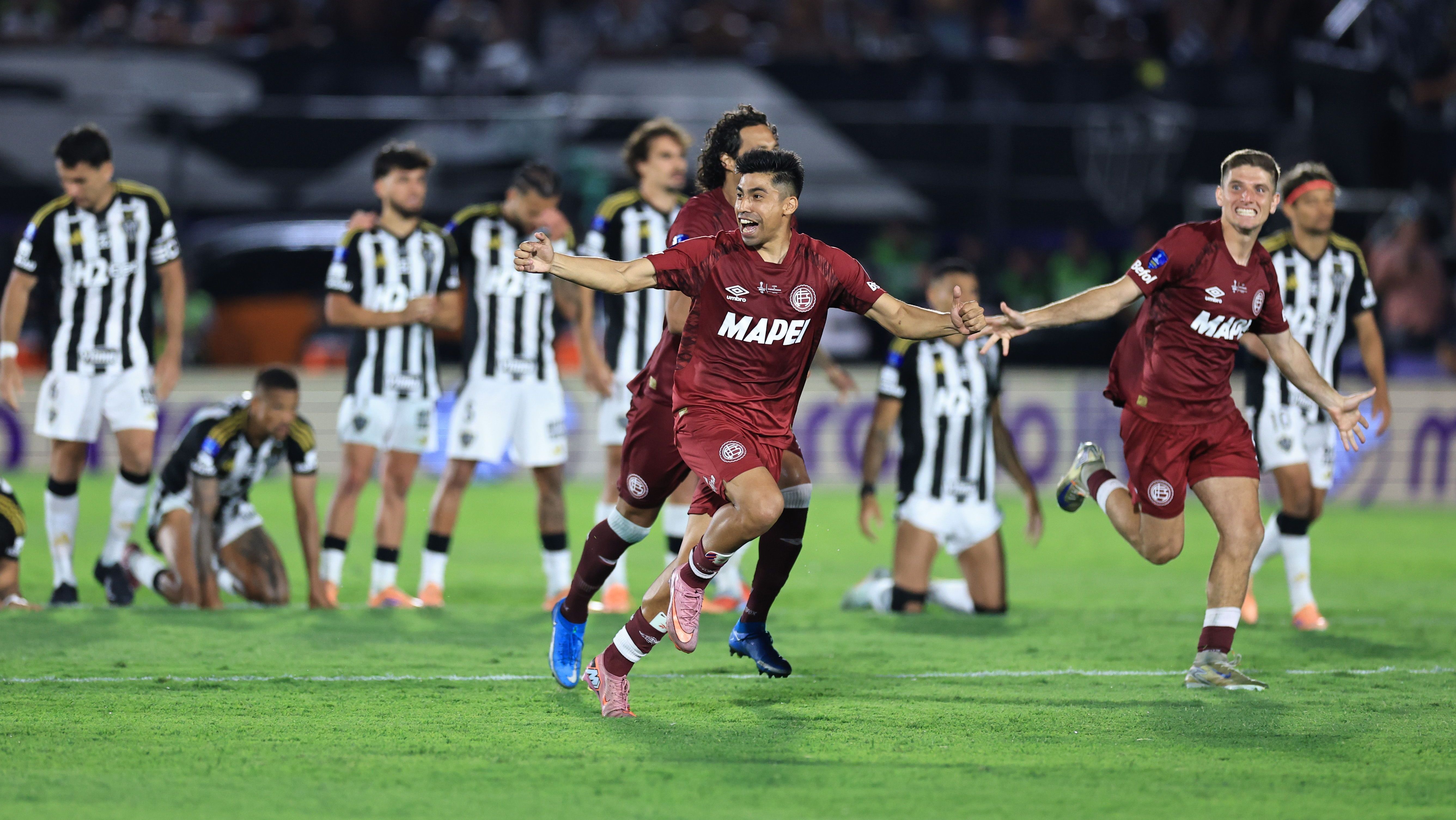 Jogadores do Lanús comemoram a vitória nos pênaltis na final na Sul-Americana, enquanto os atleticanos lamentam ao fundo