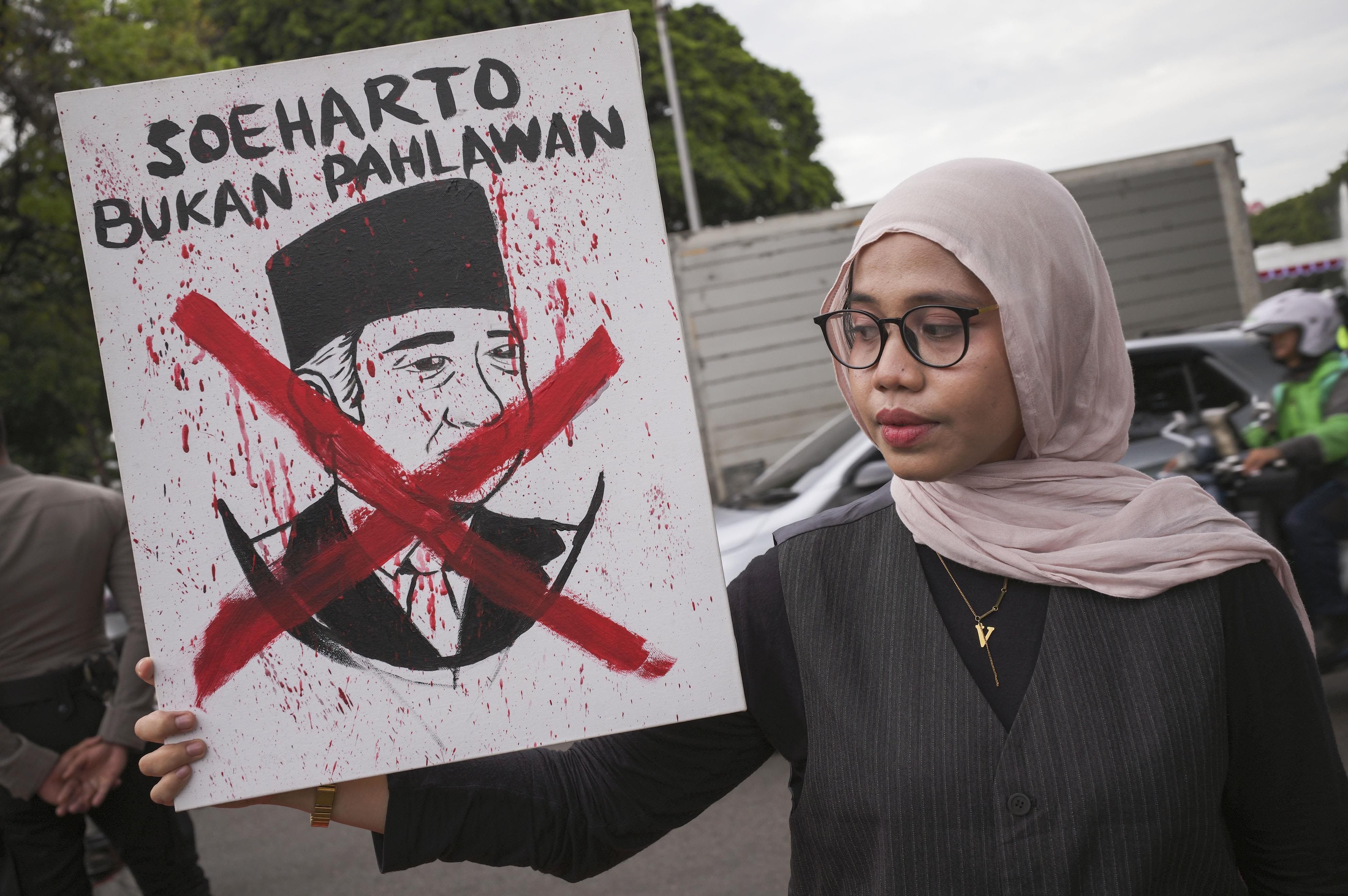 Uma mulher segura um cartaz com a imagem do falecido presidente indonésio Suharto durante um protesto contra uma proposta do governo para nomeá-lo herói nacional