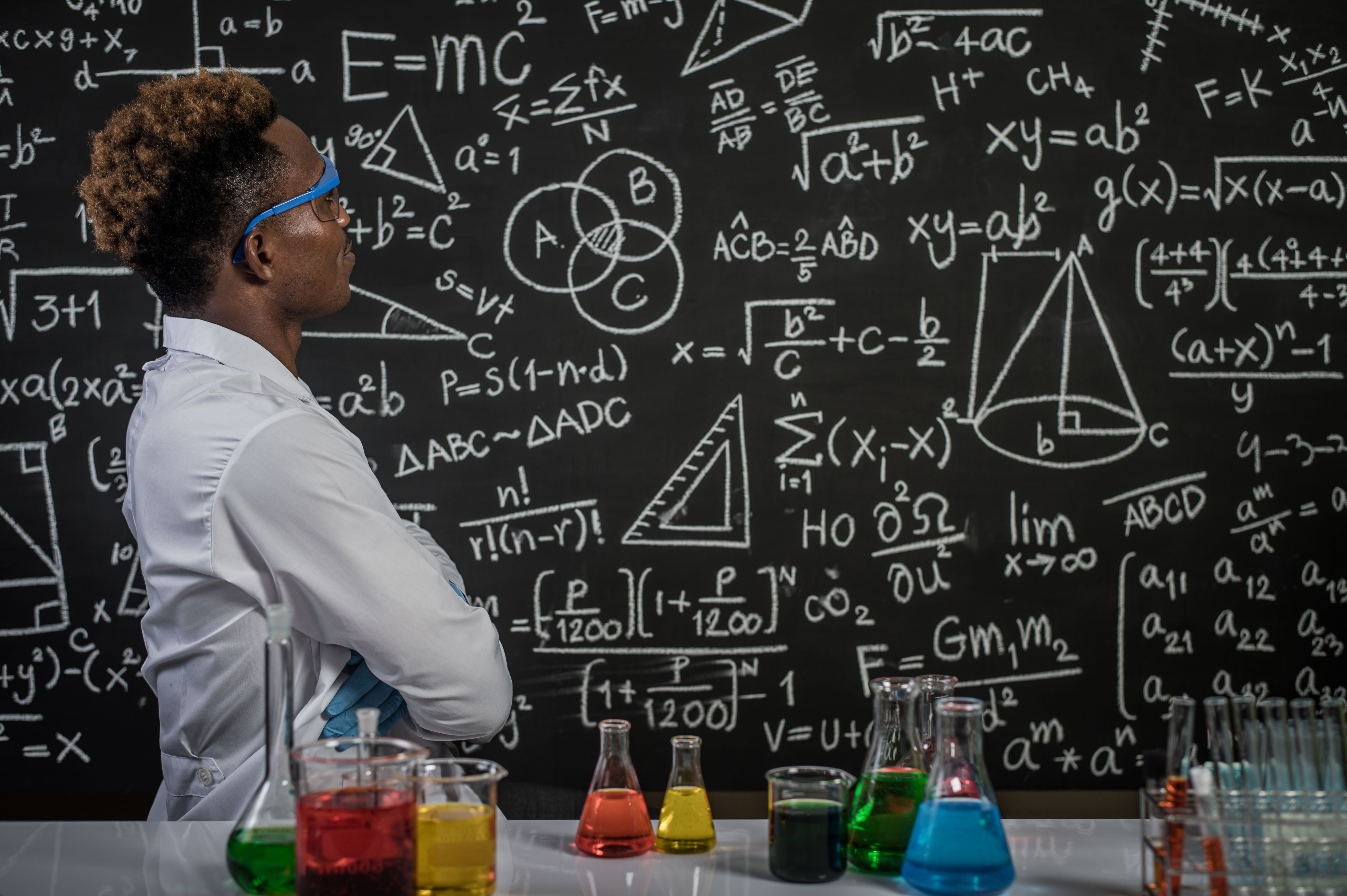 Os cientistas usam óculos e cruzam os braços para enxergar a fórmula no quadro-negro do laboratório.