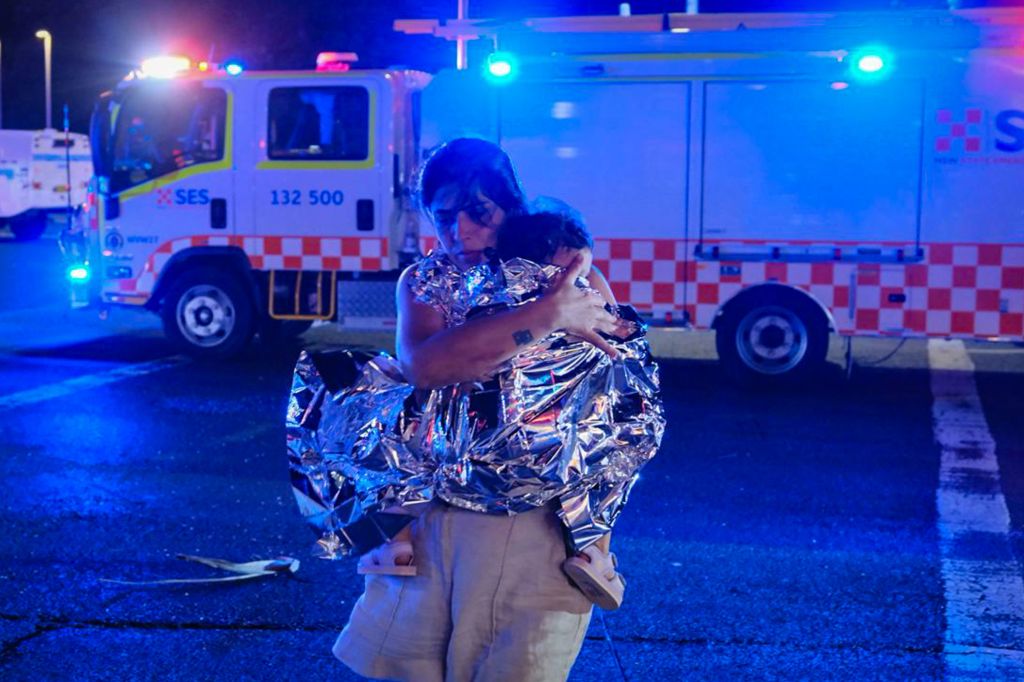 Uma pessoa deixa o local com seu filho, que está coberto por um cobertor térmico, após um tiroteio na praia de Bondi, em 14 de dezembro de 2025, em Sydney, Austrália