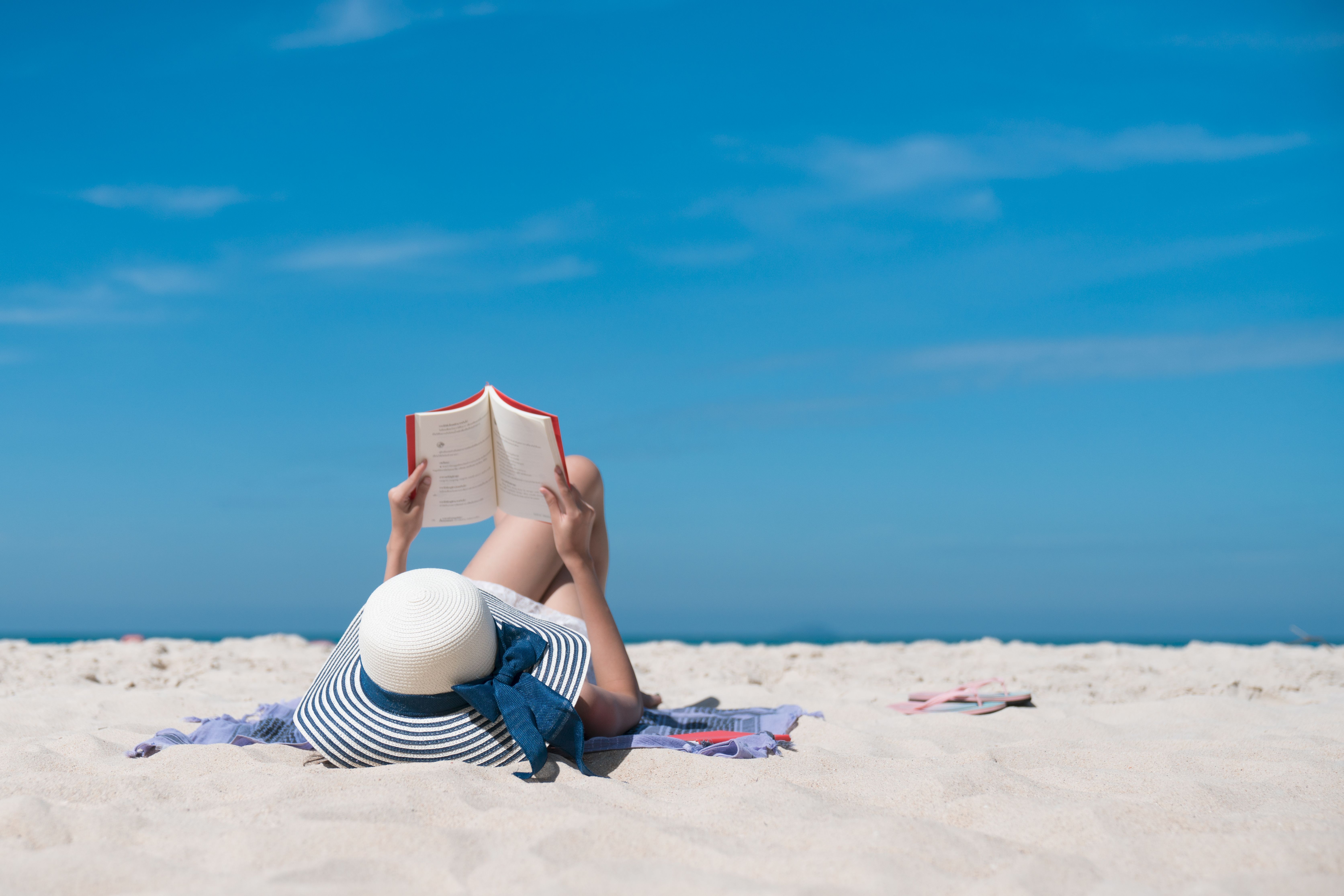 Portrait of a young brunette relaxing on the beach, reading a book
