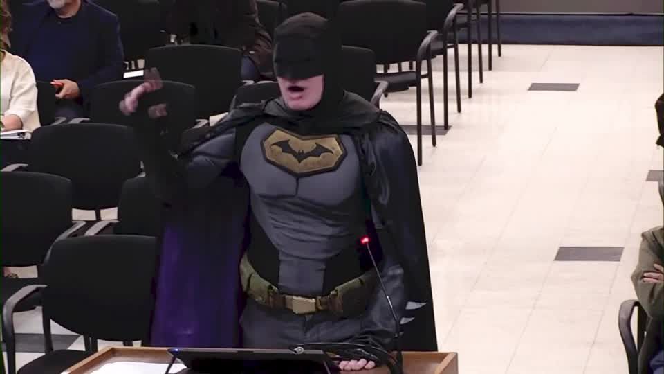 Homem fantasiado de Batman discursando em reunião do conselho municipal nos EUA